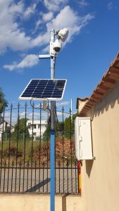 A solar panel on a pole next to a fence, equipped with sensors.